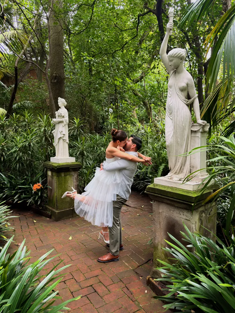 Karyme y Josué abrazados frente a frente en el jardín, entre estatuas de mármol